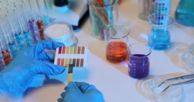 Laboratuar teknisyeni farklı çözümleri karıştıran deneyler yapar ve pH seviyelerini aynı anda incelemek için renkli test şeritleri kullanır.