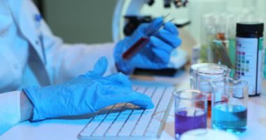 Renkli çözümlerle dolu test tüpleriyle çalışırken klavyede araştırma yapan tipler. Bilimadamı laboratuvarda kimyasal deneyleri araştırıyor..