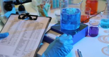 Laboratuvar teknisyeni farklı renkli çözümleri karıştırıp verileri tablete kaydediyor. Bilimadamı sıvıların kimyasal durumunu kaydediyor