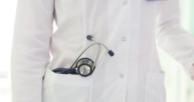 Sağlık görevlisi, cebinde steteskop saklayan, klinikte duran beyaz önlüğünü düzeltiyor. Tıbbi bakım ya da sigorta