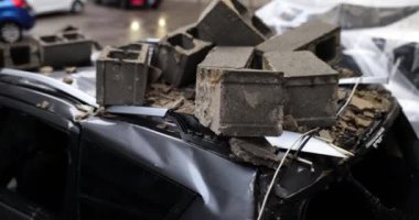 Araba, fırtına sırasında beton bloklardan düşerken hasar görmüş. Siyah otomobilin çatısı sayısız kayanın çarpmasıyla hasar gördü