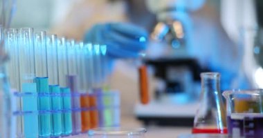 Laboratuvarda deney tüpleri ve kimyasallarla laboratuvar araştırması. Bilim adamı kırmızı turuncu sıvı ve mikroskop ile test tüpü tutuyor.