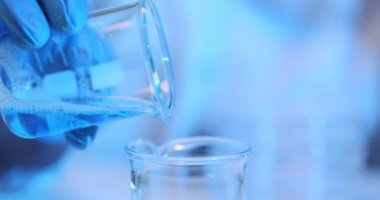 Laboratuvardaki bir deney şişesine zehirli mavi bir sıvı dökmek. Mavi solüsyonlu test tüpüne kimyasal dökülüyor.