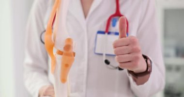 Doktor diz anatomisini açıklıyor ve baş parmak gösteriyor. Diz ve kasların anatomisi ve başarılı tedavi önerileri