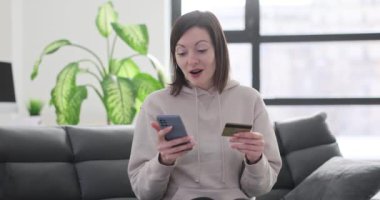 Kadın internet üzerinden akıllı telefondan satın alma onayına tepki veriyor ve kredi kartı tutuyor. Çevrimiçi ödeme başvurusu