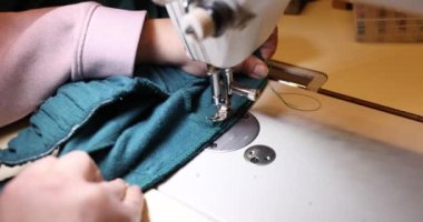 Dikiş makinesine turkuaz kumaş dikiyordu. Stüdyoda giysilerin tamiri ve terziliği