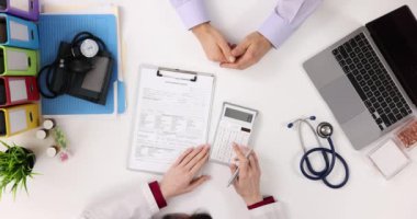 Doktor ve hasta tıbbi kayıtları ve faturaları gözden geçirir. Terapist, tedavi maliyetini hesap makinesinde hesaplar