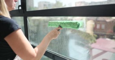 Kadın gün içinde şehir ortamında camları kazıyıcı ile yıkıyor. Pencere temizleme