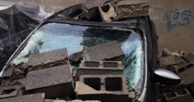 Bina çöktükten sonra hasar görmüş. Otoparktaki arabanın kaputuna tuğla bloklar.