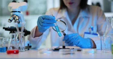 Bilim adamı laboratuarda büyüteçle mavi sıvı test tüpünü inceliyor. Zehirli sıvının incelenmesinin sonucu