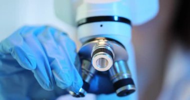 Mikroskop lenslerini ayarlayan eldiven takan bilim adamı virolog ya da doktor. Laboratuvarda çalışmak için mikroskopi ayarlanıyor