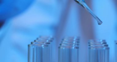 Bilim adamı laboratuardaki cam test tüplerine sıvı eklemek için bir damlatıcı kullanıyor. Kozmetik üretimi