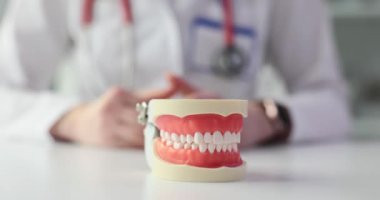 Arka planda bulanık dişçi ve dişleri koruyan bir jest olan bir masanın üzerindeki takma diş modeli. Sigortayla diş tedavisi