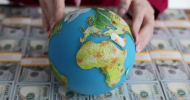 Bir yığın Amerikan dolarının üzerinde bir küreyi tutan eller. Küresel ekonomide gelir ve zenginlik