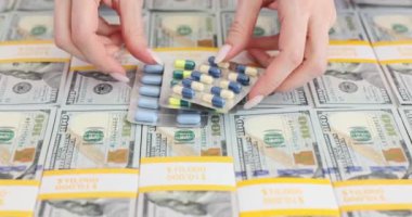 Eller tıbbî hapları 100 dolarlık banknotların üzerine koyuyor. En büyük ilaç şirketleri ve nakit gelir konsepti