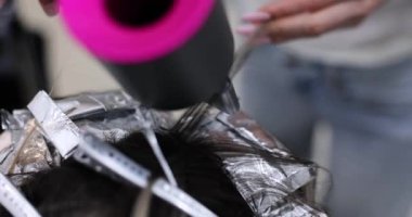 Kuaför kuaförde çamaşır suyu kullandıktan sonra saç kurutma makinesiyle saç kurutur. Güzellik salonunda saç boyama ve stil.
