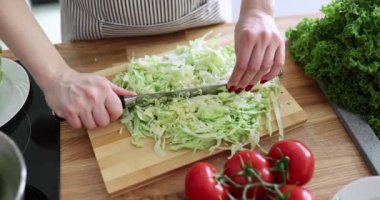 Kadın mutfaktaki tahta tahtada lahana kesiyor. Sebze salatası hazırlanıyor.