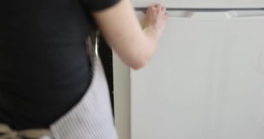 Kadın mutfakta beyaz buzdolabının kapısını açar ve bir şişe süt koyar. Süt ürünleri depolama kuralları