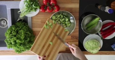 Şef, mutfaktaki ahşap kesim tahtasıyla salatalık kesiyor. Sebze salatası hazırlanıyor.