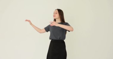 Kadın işaret dilini tek başına beyaz arka planda dans ederek gösteriyor. Kız öğrenci stüdyoda tek başına vals yapıyor.
