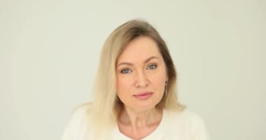 Kadın dikkatle beyaz arka plandaki kameraya bakıyor. Yoğun doğrudan bakış ve gizli sinyaller.