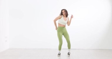 Yeşil taytlı genç bir kadın beyaz stüdyoda dans ediyor. Yaratıcı kadın modern dans koreografisini gösteriyor.