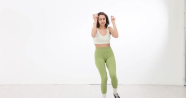 Deri elbiseli kadın beyaz stüdyoda dans adımları atıyor. Hazır kadın, beyaz arka planda temel afro hareketleri yapmaya başlıyor.