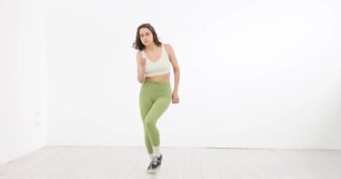 Yeşil taytlı kadın dans figürleri yapıyor ve beyaz arka planda zıplıyor. İçeride dans eden zarif bir kadın.