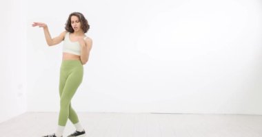 Yeşil taytlı kadın beyaz odada dans ediyor. Spor dansı ve sağlık