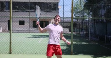 Erkek güneşli bir günde tenis maçını kazanmayı kutlar. Başarılı tenis ve mutlu duygular oyunu
