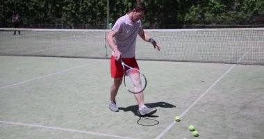 Tenisçi, sahada raket tutarak alnını siler ve sahada top toplar. Yorgun tenisçi sahadan ayrılıyor.