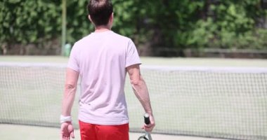 Erkek tenisçi güneşli bir günde tenis kortunda yürür. Tenis oyunu