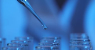Laboratuvar çalışanı cam test tüplerine mavi sıvı örnekleri döküyor. Laboratuvarda cam test tüpleri kullanılarak gösterilen hassas pipet tekniği