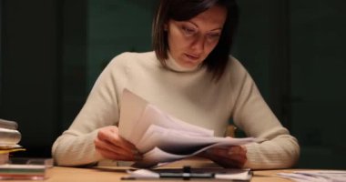 İş kadını ya da denetçi akşamları çalıştığı yerde otururken belgeleri inceler. Genç bayan çalışanlar gece ofiste finansal işlemleri ayrıntılı bir şekilde gözden geçirirler.