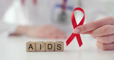 Doktor elinde AIDS ve HIV 'den korunmak için uluslararası günün kırmızı kurdelesini tutuyor. AIDS konusundaki farkındalık ve eğitimin artırılması