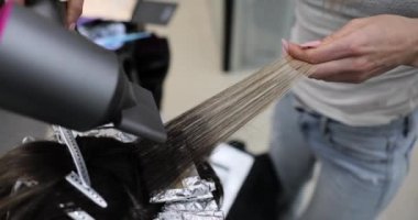 Profesyonel saç boyama tekniğinin bir kuaför salonunda gösterimi. Kuaför saç boyama yaparken saç kurutma makinesi kullanır.