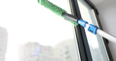Ofisinde yeşil bir kazıyıcı olan yüksek katlı bir binanın camlarını silmek. Çalışkan kadın kusursuz bir şekilde parlayana kadar pencereyi dikkatlice siler. Pencere temizleme