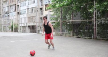 Genç adam futbol yeteneklerini şehir parkındaki beton sahada geliştiriyor. Futbol oyunu