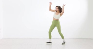 Beyaz arka planda dans eden güzel bir genç kadın. Ritmik hareketler ve enerjik ifadelerle dans rutini