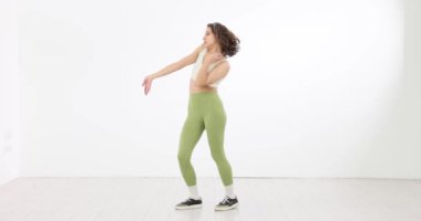 Beyaz arka planda dans eden güzel bir genç kadın. Stüdyoda yaratıcı hareketleri gösteren dans gösterisi