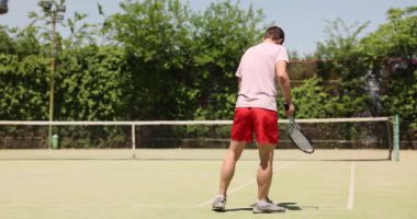 Tenis oyuncusu güneşli bir günde kortta antrenman yapıyor. Tenis kortuna ayak basan bir sporcu. Top ve tenis raketiyle. Tenis oyunu