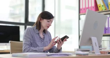 Akıllı telefon kullanan genç bir kadın müşteriyle iletişim kuruyor ve ofiste notlar yazıyor. Çoklu görev yapan kadın elinde akıllı telefon ve rapor tutuyor.