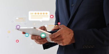 İşadamı elinde yüzen dijital inceleme simgeleriyle tablet kullanıyor. Uygulamalar ve web siteleri için beş yıldızlı ürün değerlendirme simgesi.