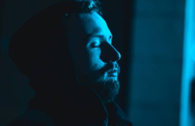 Karanlıkta kapüşonlu, soğuk mavi ışıklı, sigara içen yakışıklı bir adamın portresi. Neon modern bir şehirde gece hayatı genç adam..
