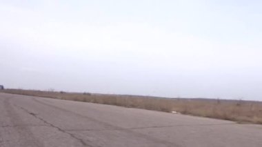 Havalı, havalı, deri ceketli bir adamın asfalt bir yolda klasik motosikletini sürüşünün arka planda, sonbahar bulutlu bir akşamda çıkan ateşle yan görüntüsü..