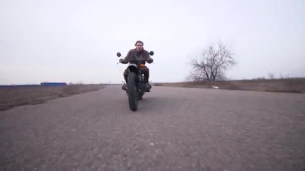 老旧摩托车上年轻的争吵者从低角度出发 从远处射击 骑得越来越近了 秋末凄凉无色的乡间景色 — 图库视频影像