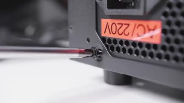 Tight the bolt using a crosshead screwdriver, assembling the computer power supply unit after repair. Close filmed computer hardware technician work process at the service.