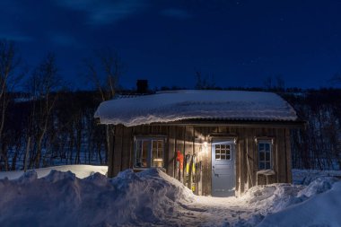 Sıcak Wintry Kayak Tatil Köyü Karlı Çatı ve Kuzey İsveç Ormanları 'ndaki açık mavi gökyüzü ile aydınlatılmış Pencereler.
