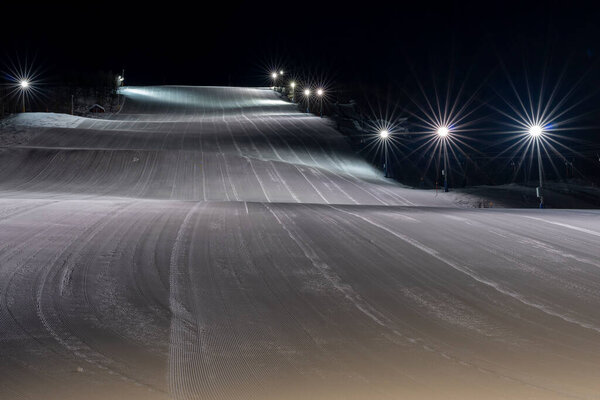 Nighttime at the Illuminated Ski Slope in Ramundberget Resort area in Sweden with empty Slopes and no Skier in newly Groomed Piste.