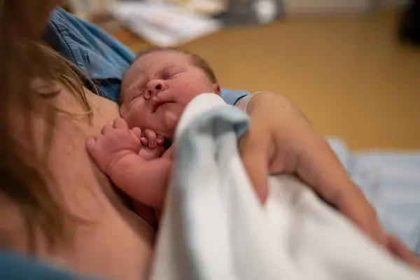 stock image A touching scene of a newborn baby wrapped in a white blanket, being held close by a parent in a hospital room. The tender care and bonding during the first moments of life.